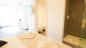 Una habitación de hotel moderna con cama, ducha con mampara de vidrio y vista al baño.