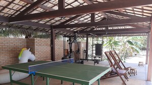 Een overdekt buitengebied met een tafeltennistafel, fitnessapparatuur en zitplaatsen.