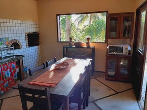 Cozinha com painel de azulejos, forno embutido, janela com vista para o verde, micro-ondas e armário com louças.