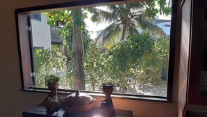 Een raam met uitzicht op een tropische tuin, met bomen en een palmboom.