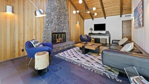 Ein modernes Wohnzimmer mit Kamin aus Stein, Holzbalkendecke und einem großen Flachbildfernseher.