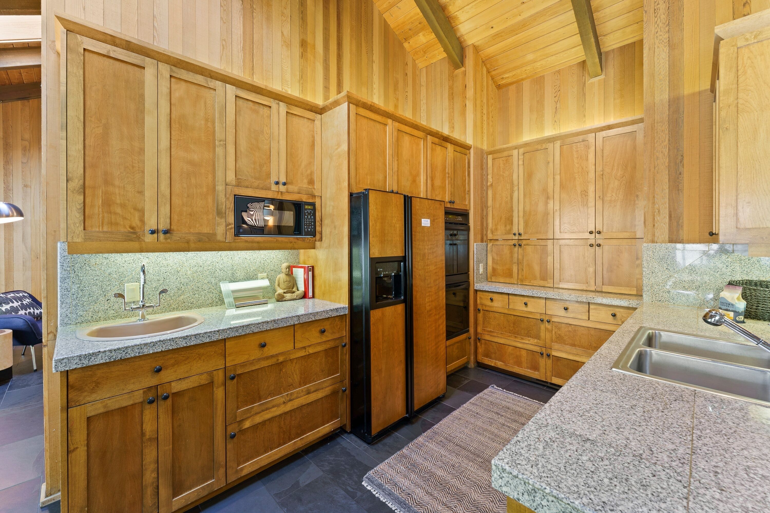 A kitchen with wooden cabinets, granite countertops, a refrigerator, a microwave, and a sink.