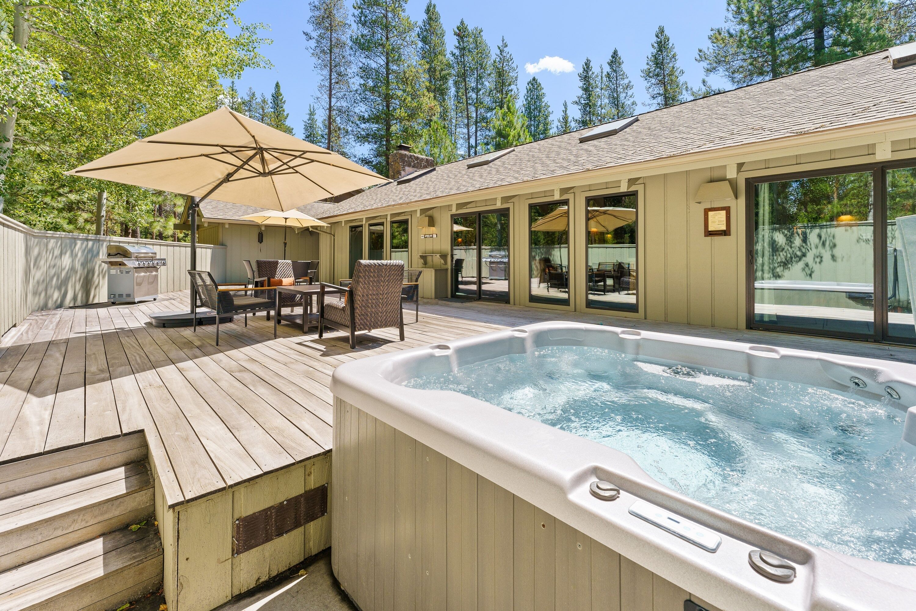 A hot tub with a wooden deck, outdoor seating, and a covered patio area.