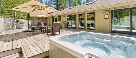 A hot tub with a wooden deck, outdoor seating, and a covered patio area.