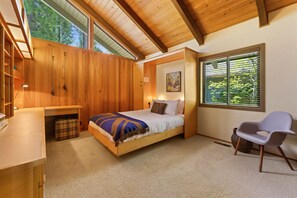 A bedroom with a wooden bed, a desk, a chair, and a window with blinds.