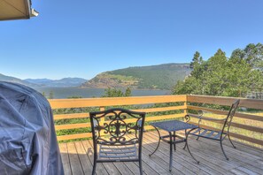 A wooden deck with a metal table and chairs, overlooking a lake and mountains. - Amber Sunset 3 Bedroom Home by RedAwning (Mosier)