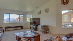 Ein Wohnzimmer mit großem Fenster, Flachbildfernseher, Kamin und gemütlicher Sitzecke.