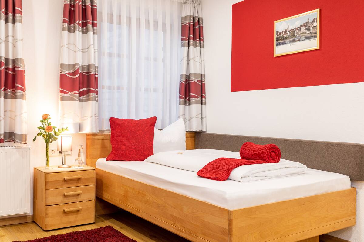 Une chambre à coucher avec un lit en bois, des oreillers rouges, une couverture rouge, une table de chevet avec une lampe et un tableau encadré au mur.