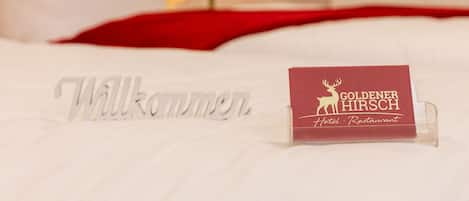 A bed with a welcome sign and a business card for the Goldenner Hirsch Hotel and Restaurant.