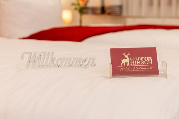 A bed with a welcome sign and a business card for the Goldenner Hirsch Hotel and Restaurant.