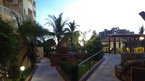A paved pathway leading to a building with a palm tree and a small rock formation.