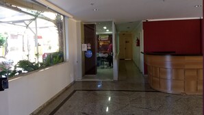 A hallway with a reception desk, a glass door leading to a restaurant, and a tiled floor.
