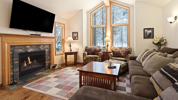 A living room with a fireplace, a television mounted on the wall, and a large window with a view of trees. - 9 Hoodoo Home with XBOX 360 and Private Hot Tub by RedAwning (Bend)
