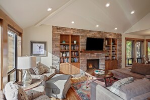 Un salon chaleureux avec une cheminée en pierre, une bibliothèque et des fauteuils confortables.