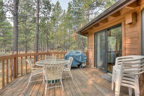 A wooden deck with a table and chairs, a barbecue grill, and a sliding glass door leading to a cabin.