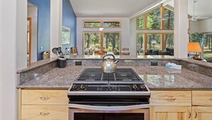 A modern kitchen with a granite countertop, stainless steel stove, and large windows offering a view of the outdoors. - 1 Colonial Private Family Vacation Home features Bikes to Explore Sunriver by RedAwning (Bend)