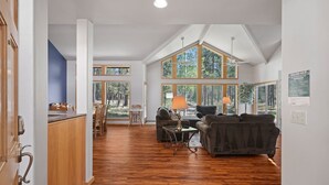 A spacious living area with a high ceiling, large windows, and a kitchen area visible in the background. - 1 Colonial Private Family Vacation Home features Bikes to Explore Sunriver by RedAwning (Bend)