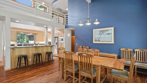A spacious dining area with a wooden table and chairs, a kitchen in the background, and a blue accent wall with a framed picture. - 1 Colonial Private Family Vacation Home features Bikes to Explore Sunriver by RedAwning (Bend)