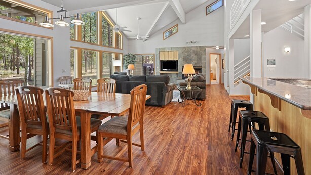 A spacious living area with a dining table, wooden chairs, a sofa, and a kitchen area with a TV and bar stools. - 1 Colonial Private Family Vacation Home features Bikes to Explore Sunriver by RedAwning (Bend)