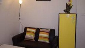 Una habitación con un sofá negro, un refrigerador amarillo y una lámpara fijada a la pared.