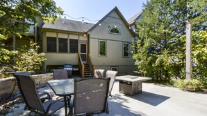 An outdoor patio with a dining set, a stone wall, and a house in the background. - Elite Escape-2 POOLS, Splash Pad, PoolTable, Hot Tub, Patio w/Fire Pit+Fireplace (Hollister)
