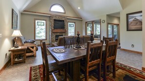 A dining area with a high ceiling, stone fireplace, and large windows. - Elite Escape-2 POOLS, Splash Pad, PoolTable, Hot Tub, Patio w/Fire Pit+Fireplace (Hollister)