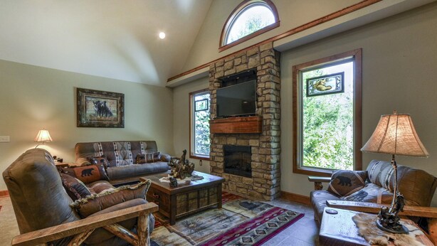 A cozy living room with a stone fireplace, comfortable seating, and large windows. - Elite Escape-2 POOLS, Splash Pad, PoolTable, Hot Tub, Patio w/Fire Pit+Fireplace (Hollister)