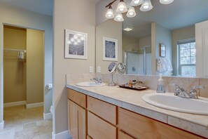 Features two sinks, a large mirror, and a walk-in shower with a glass door.