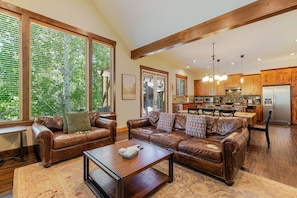 A spacious living area with leather sofas, a coffee table, and large windows with blinds.