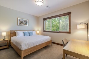A bedroom with a wooden bed, a nightstand, a desk, a chair, a window with blinds, a wall-mounted lamp, and a framed picture. - Points West 4 Bedroom Townhouse by RedAwning (Bend)