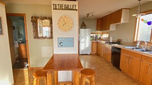 A kitchen with wooden flooring, a wooden dining table with stools, a wall clock, and a sign that reads "TO THE GALLEY". - Relaxing Elevated Lake House Retreat (Mayville)