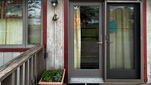 A building with a red roof, a gray door with a glass panel, a wooden porch, and a planter box with green plants. - Relaxing Elevated Lake House Retreat (Mayville)
