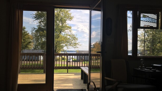A room with a sliding glass door leading to a backyard with a wooden deck and a bench. - Relaxing Elevated Lake House Retreat (Mayville)