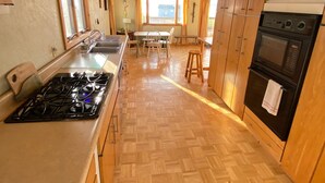 A kitchen with wooden cabinets, a gas stove, an oven, and a dining area with a table and chairs. - Relaxing Elevated Lake House Retreat (Mayville)