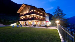 Un edificio grande de varios pisos con un balcón, una zona de estar al aire libre y una entrada bien iluminada.