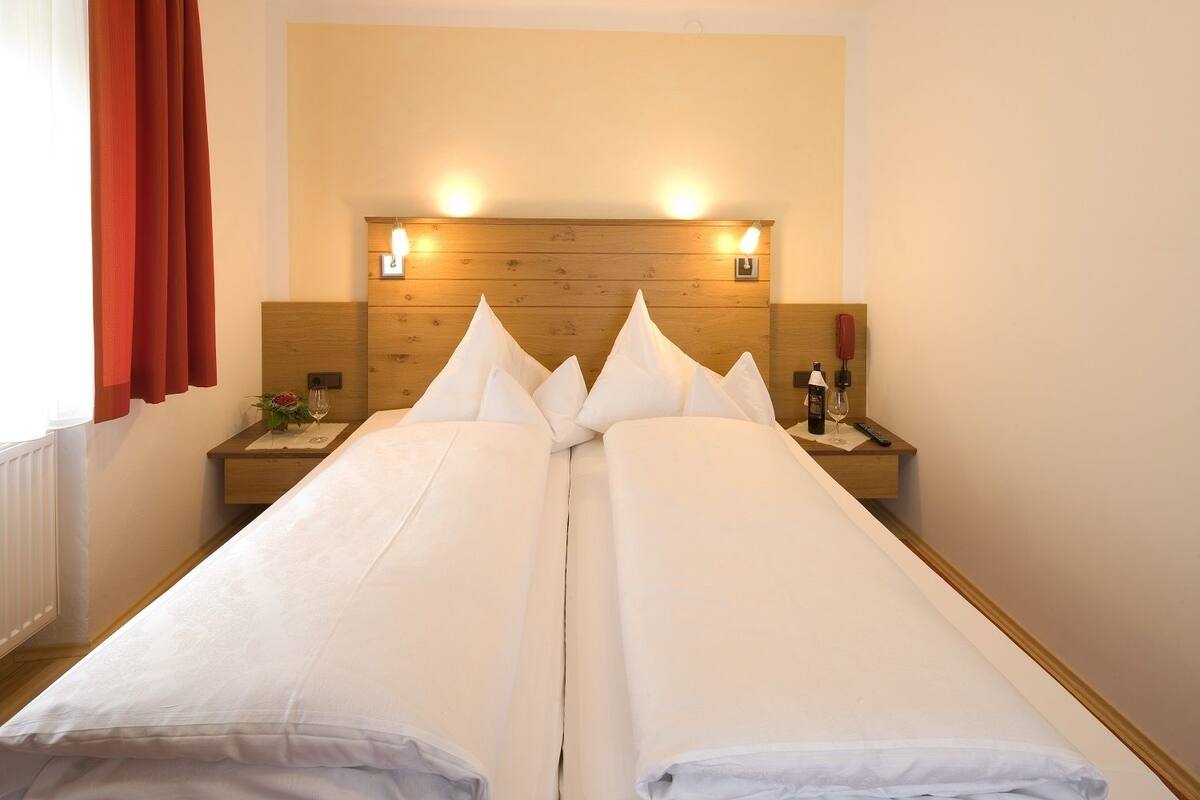 Una cama doble con ropa de cama blanca, cabecera de madera, mesitas de noche con lámparas y un teléfono rojo.