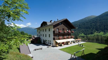 Ein zweigeschossiges Gebäude mit einem Balkon, einer gepflasterten Terrasse und Blick auf Berge.