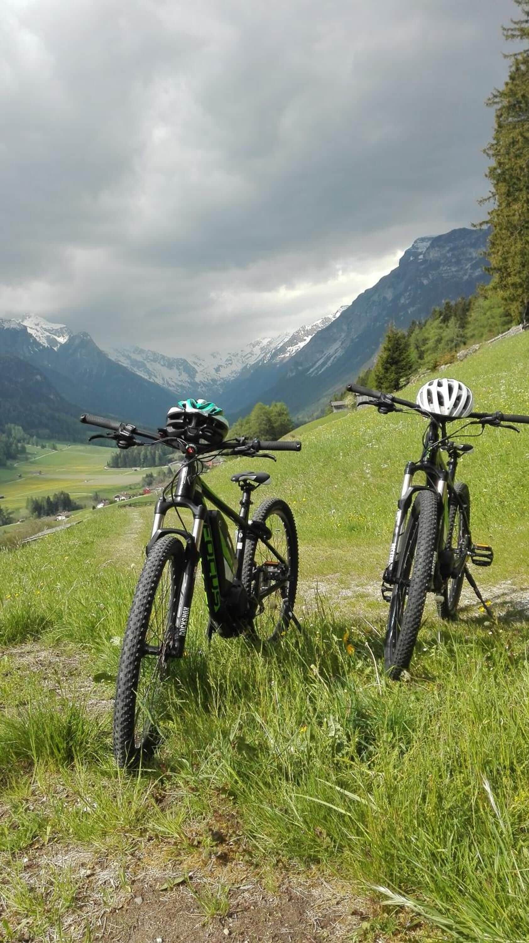 Two mountain bikes parked on a grassy hillside with a mountainous landscape in the background.