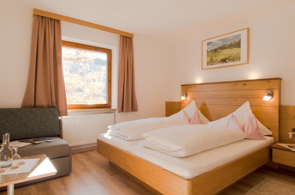 Un dormitorio con cama de madera, una mesita de noche, una ventana con cortinas y un cuadro enmarcado en la pared.