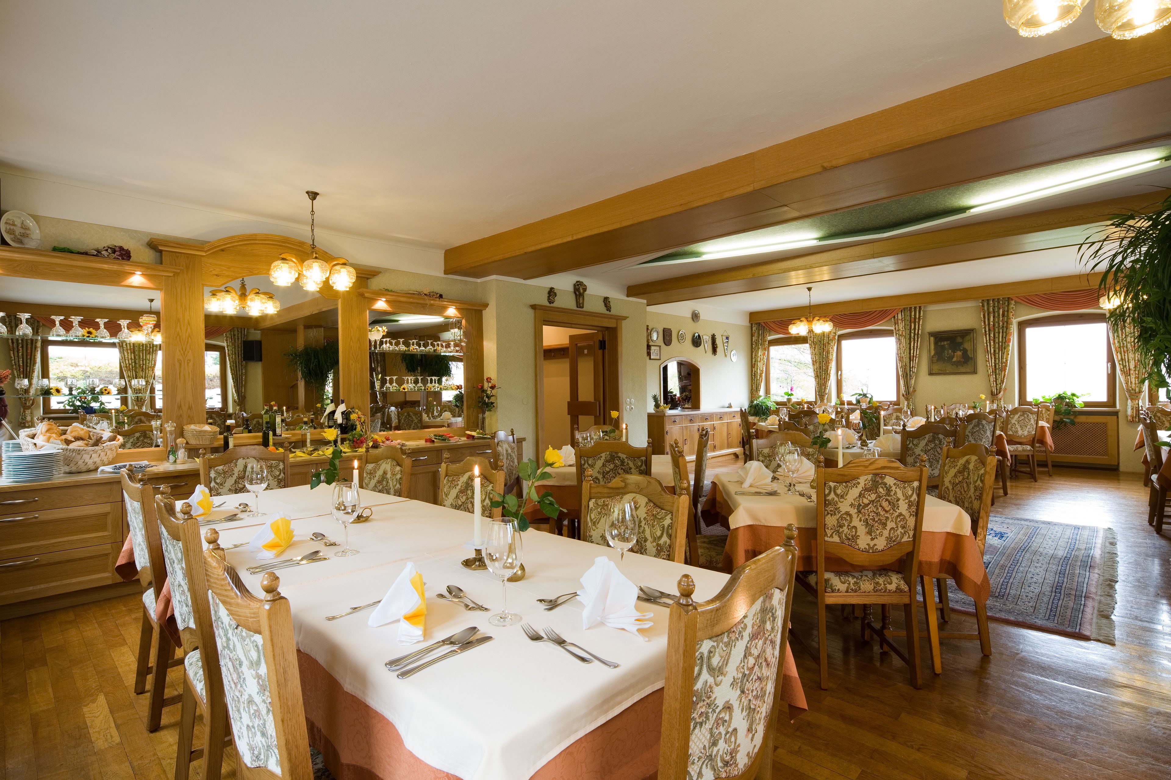 A spacious dining area with multiple tables set for service, wooden chairs, and a warm, inviting atmosphere.