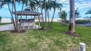 A gazebo with a grill, surrounded by palm trees and a grassy area. - Beautiful Beachfront condo with Gulf View FALL SPECIAL 20% OFF ANY RES TIL 10/31 (Fort Myers Beach)