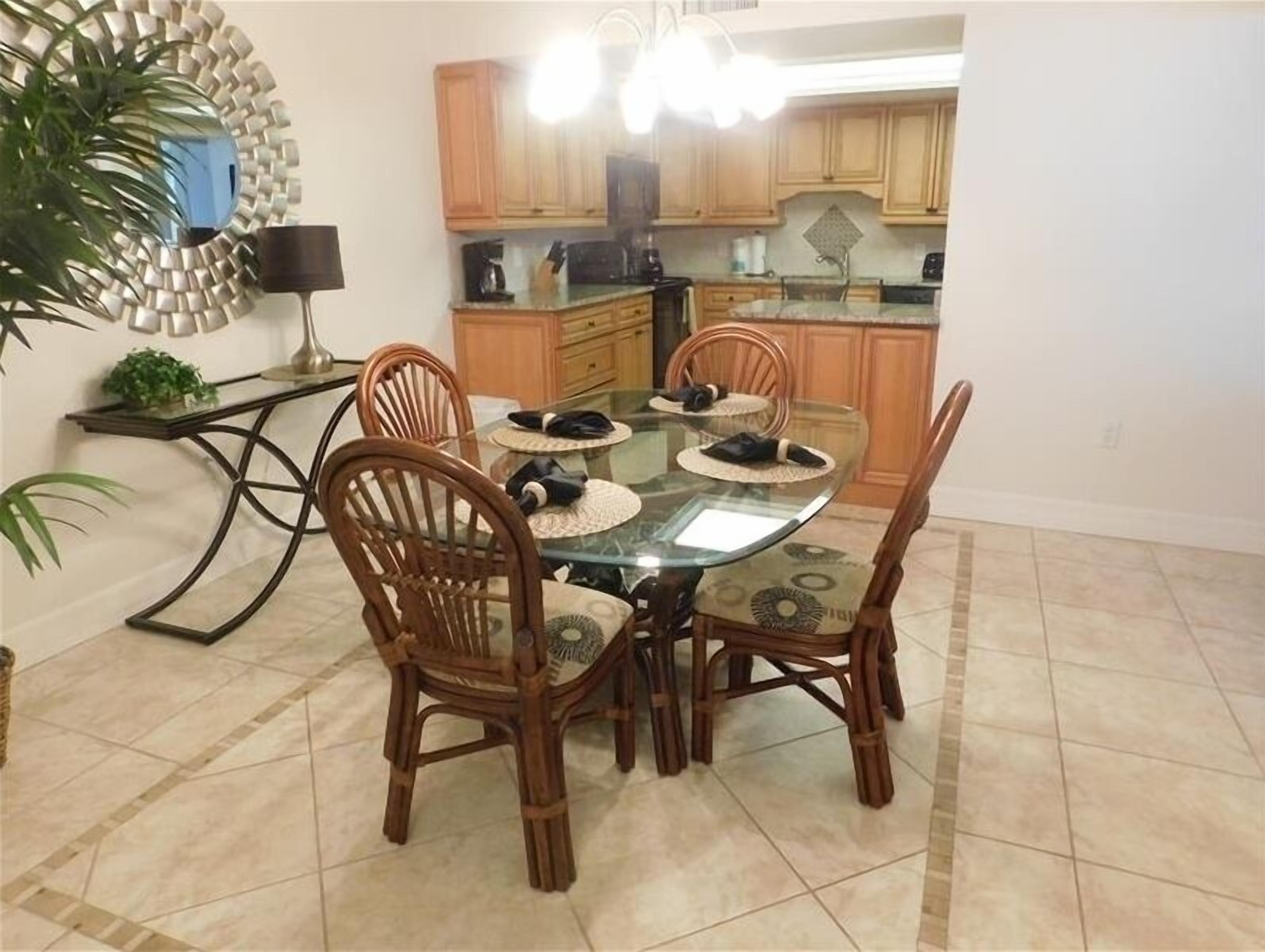 Un comedor con una mesa de vidrio rodeada de sillas de madera, una cocina al fondo y un adorno decorativo en la pared.