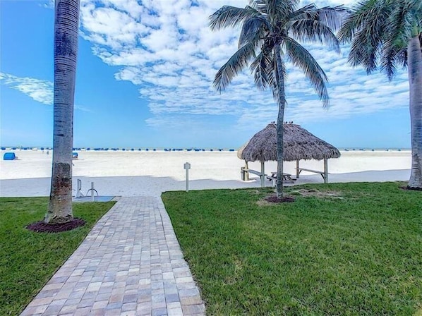 A pathway leading to a beach with a thatched structure and palm trees.