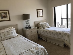 A bedroom with two beds, a nightstand, a lamp, and a window with a view.