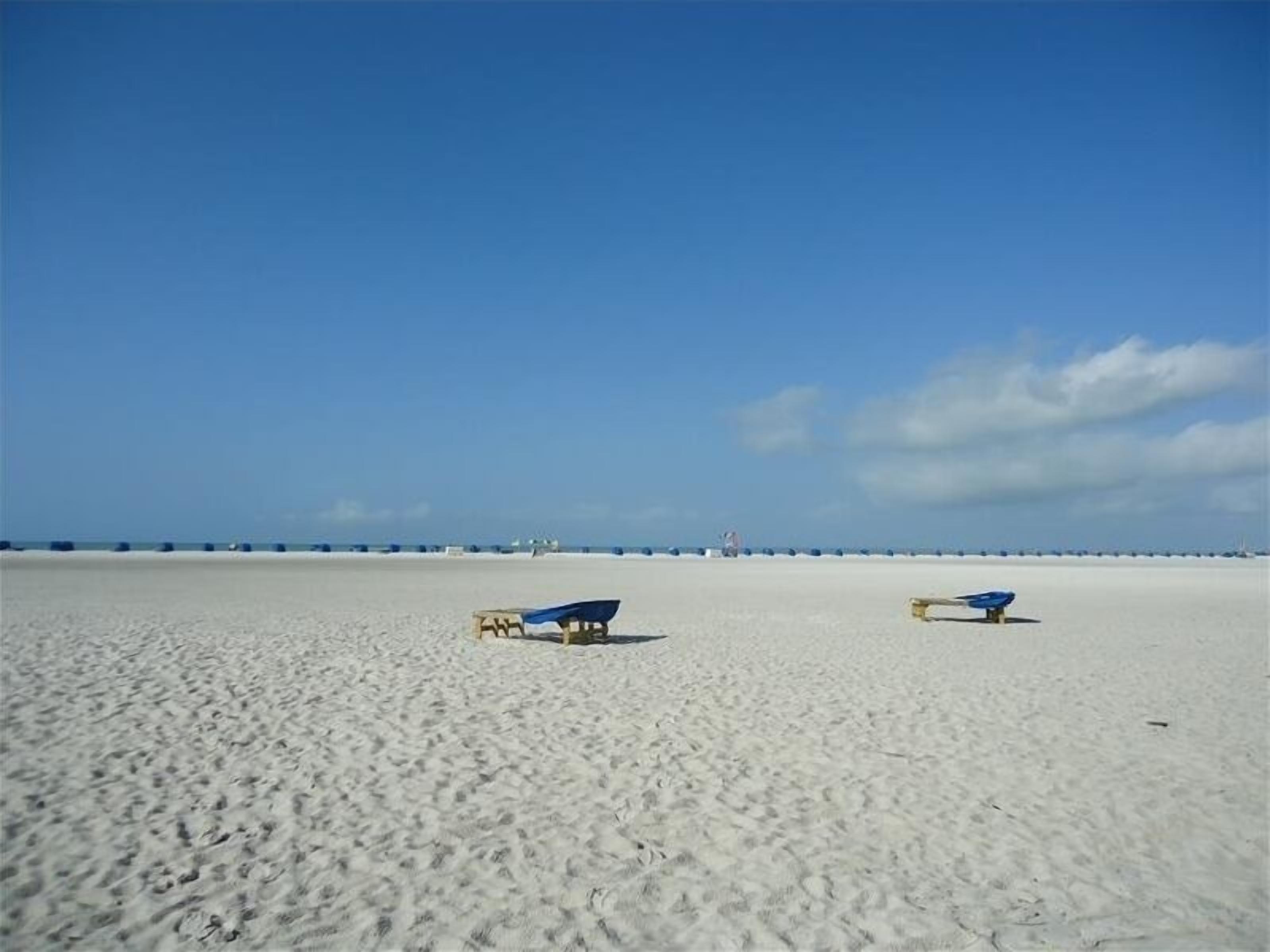 Ein Strand mit zwei blauen Liegestühlen und einem gelben Sonnenstuhl im Sand.