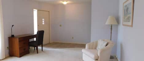 Una habitación con escritorio, silla y sofá. Se ve una puerta y una lámpara en el techo.
