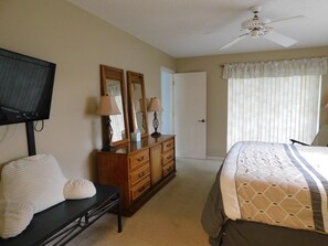 Une chambre à coucher comprenant un lit, une commode, un téléviseur et un ventilateur de plafond.