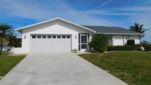 A single-story house with a garage, a front lawn, and a clear sky. - That One Particular Harbor - Gulf Access Pool Home  3/2 (Cape Coral)