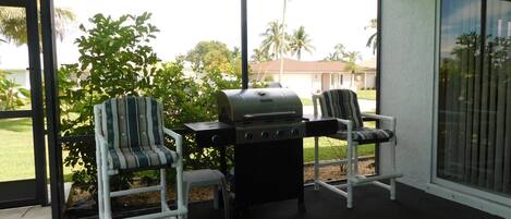 A covered patio area with two chairs and a grill.