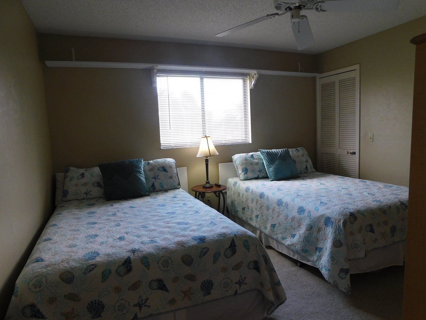 A bedroom with two beds, a window with blinds, a ceiling fan, and a door.